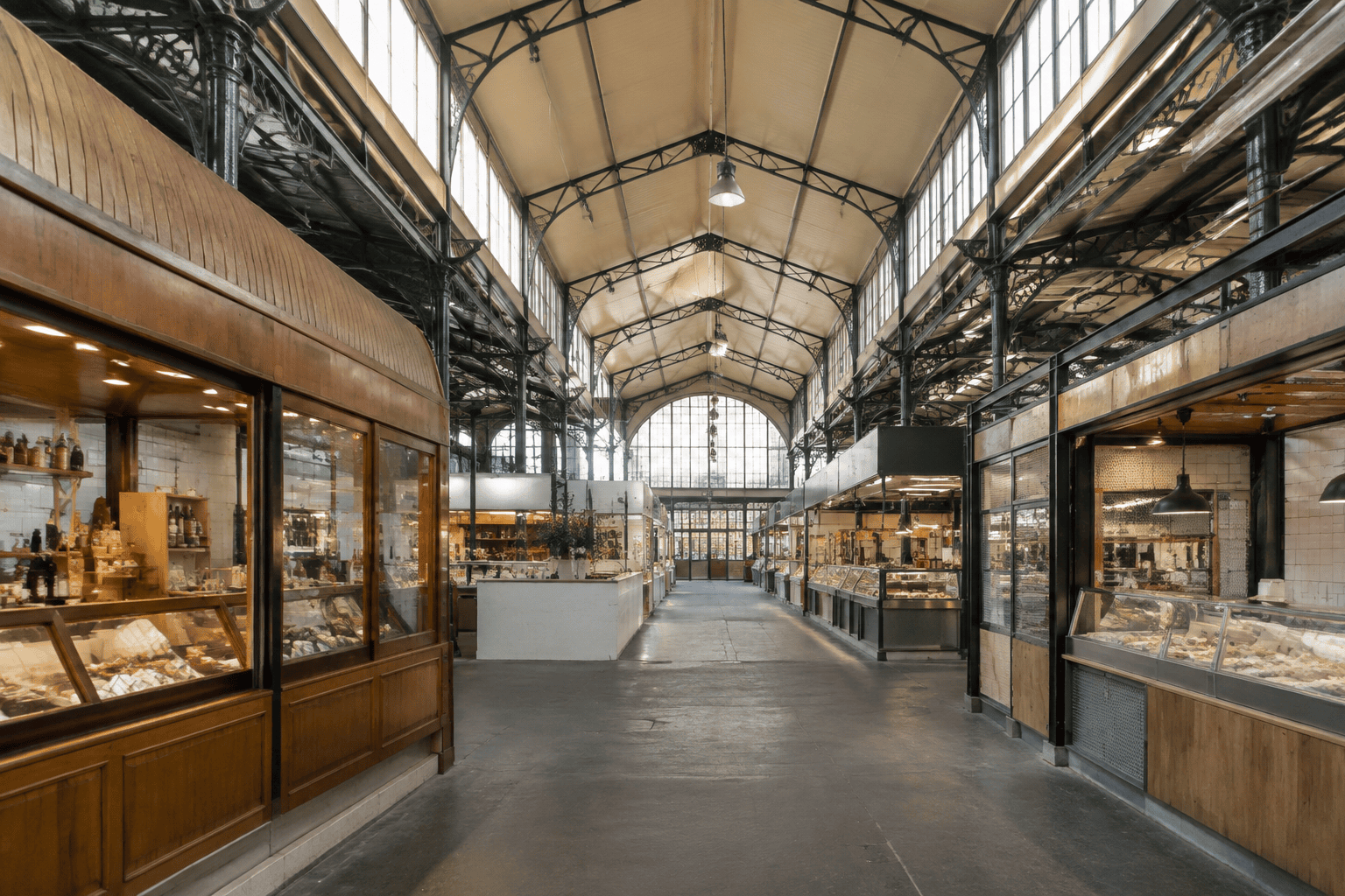 Allée centrale sous la charpente d’une halle couverte, bordée de commerces et d’étals.