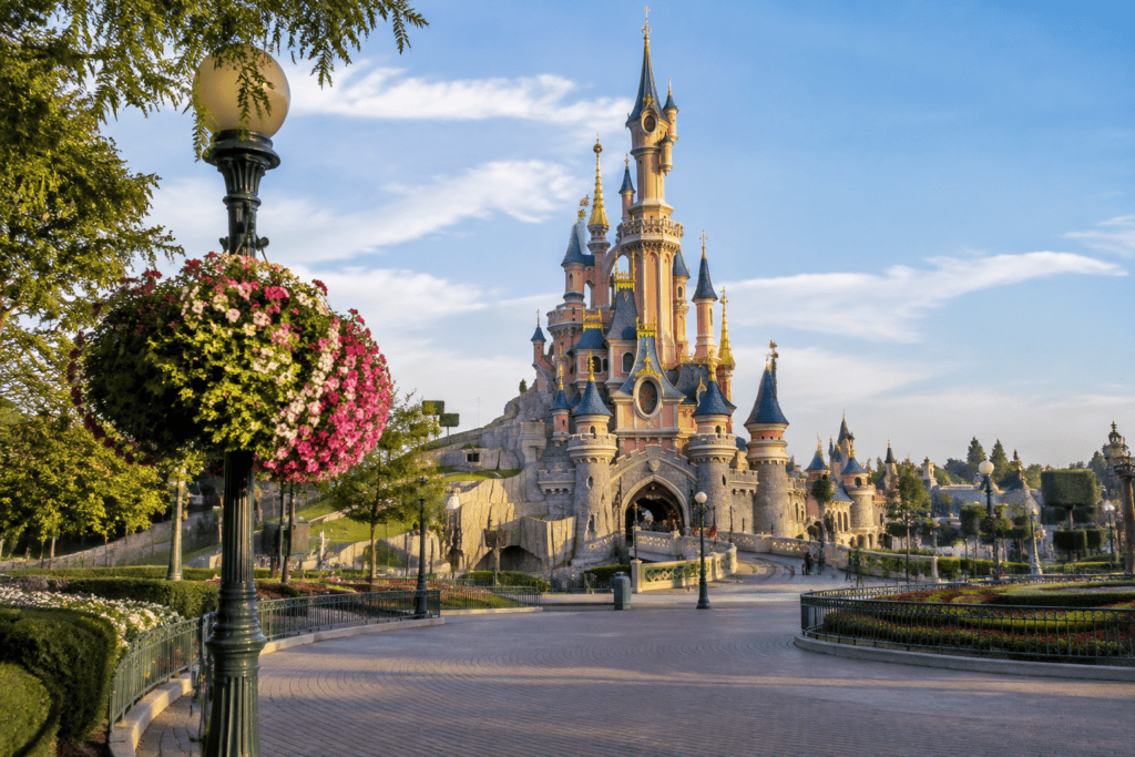 Le château rose et bleu de Disneyland Paris au bout d’une allée bordée de jardins.