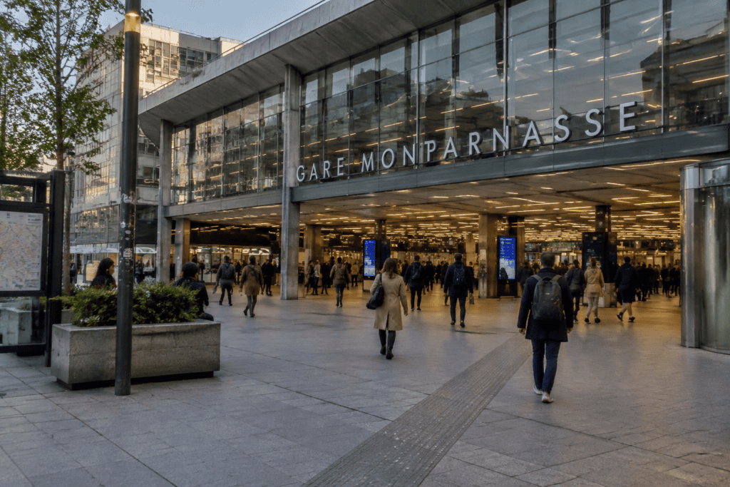 Façade vitrée de la gare Montparnasse et voyageurs sur le parvis.