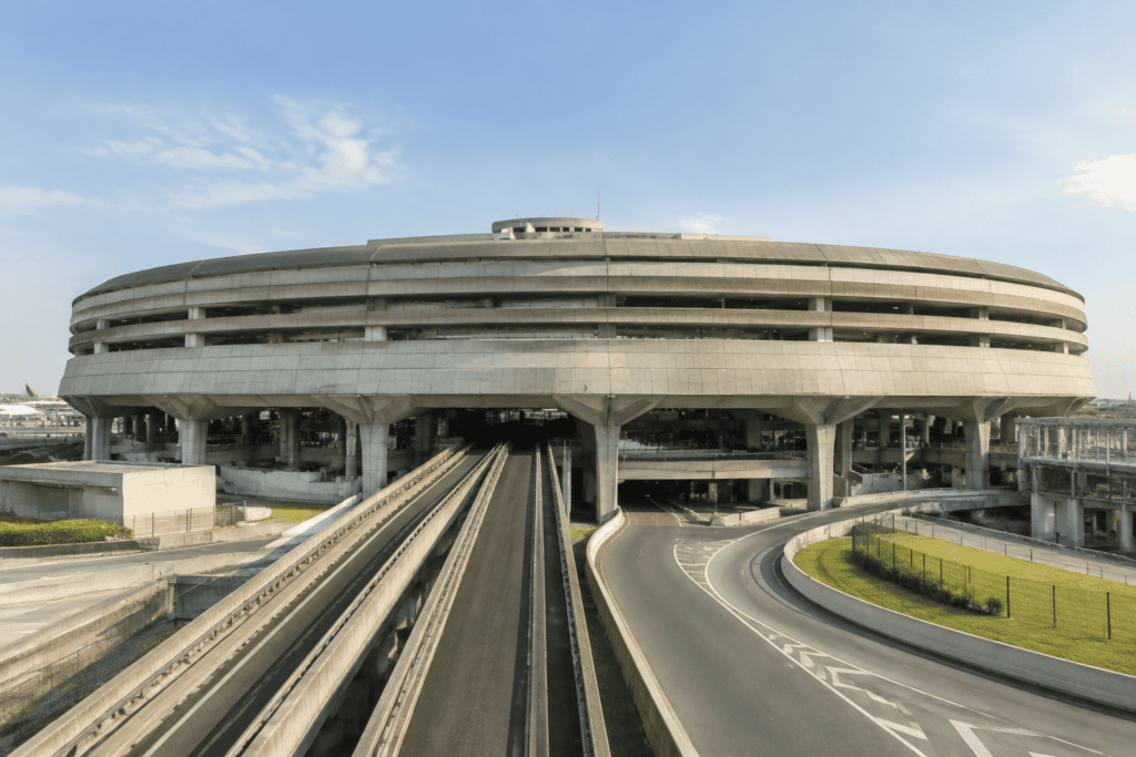 Bâtiment circulaire du terminal 1 de CDG au-dessus de voies ferrées et d’une route d’accès.