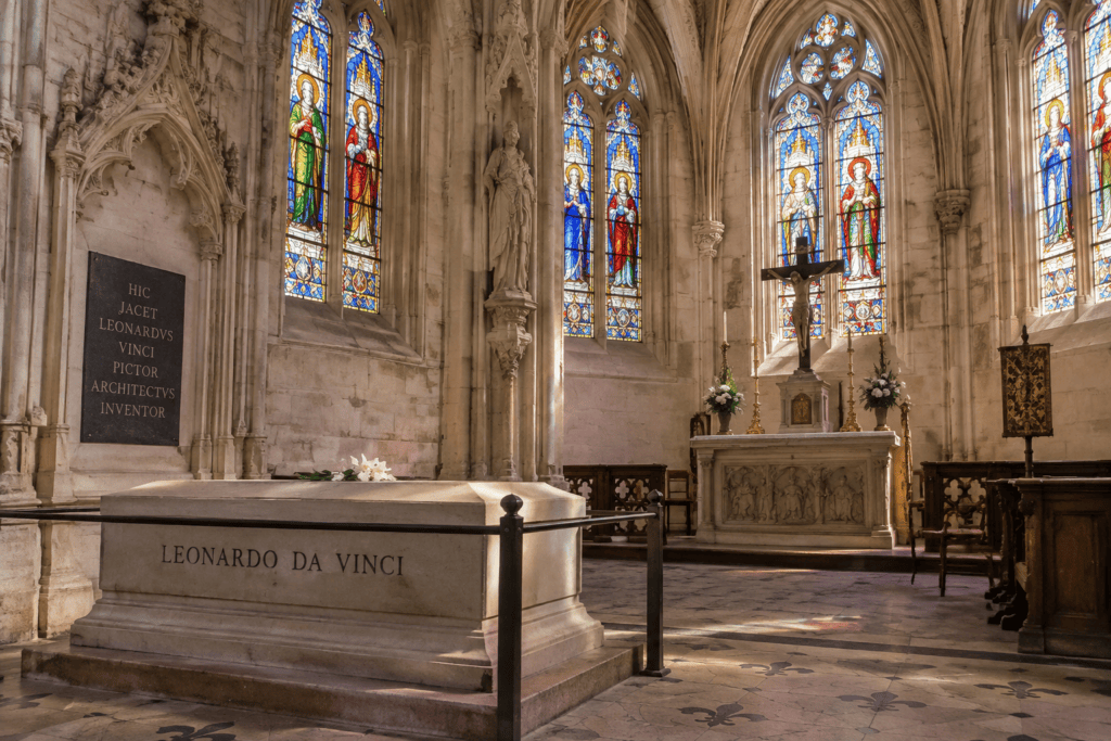 Dans la chapelle Saint-Hubert, un tombeau portant le nom de Léonard de Vinci se trouve devant des vitraux colorés et un autel.