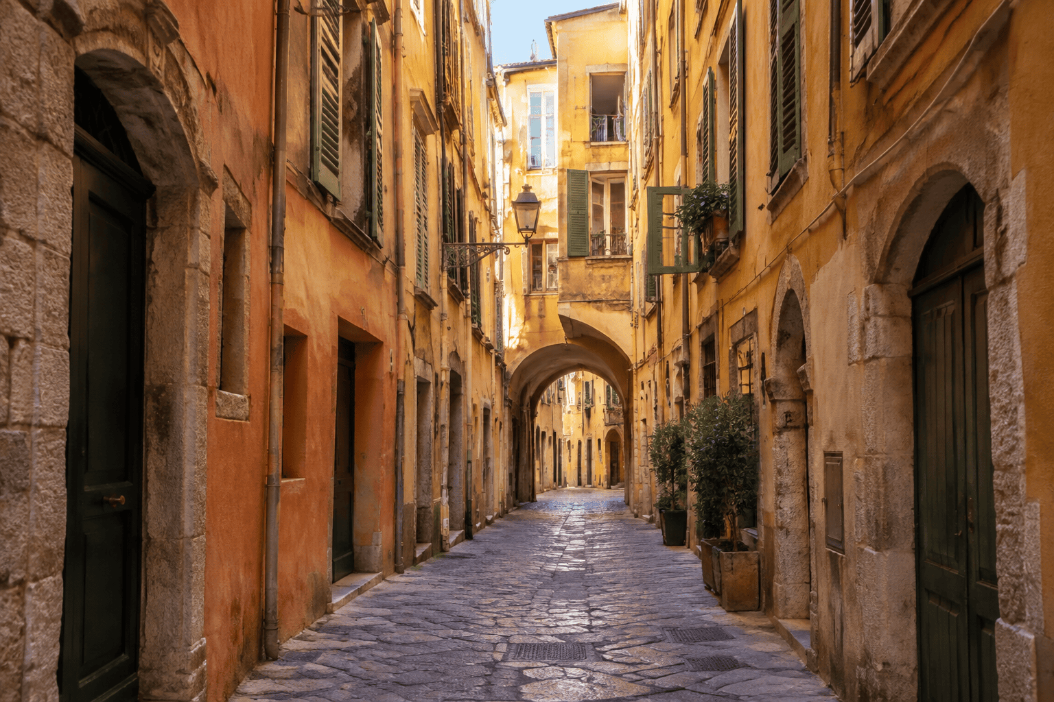 Ruelle pavée bordée de hautes façades ocre, avec un passage voûté au loin.