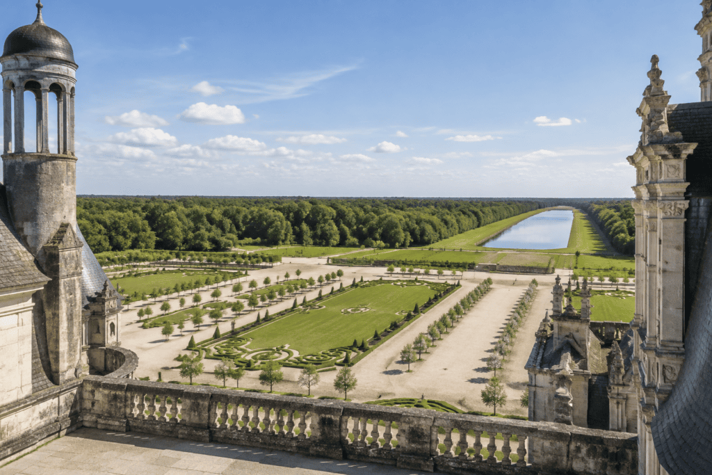 Depuis une terrasse en pierre, vue sur les jardins réguliers et la forêt au-delà du château.