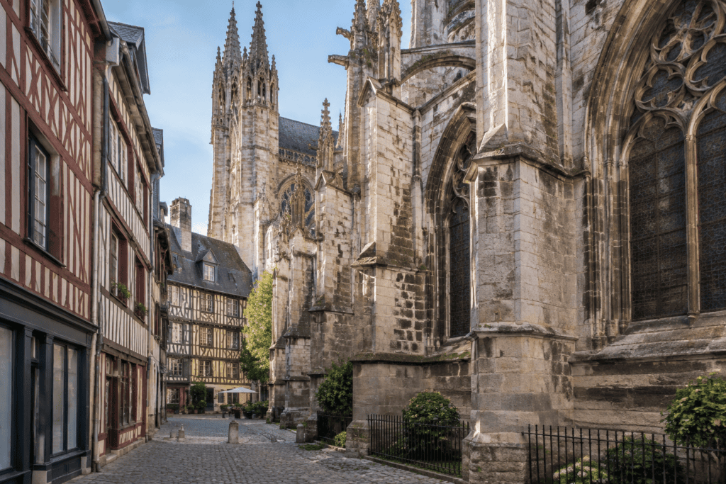 Les contreforts et les fenêtres gothiques de la cathédrale bordent une ruelle pavée bordée de maisons à pans de bois.