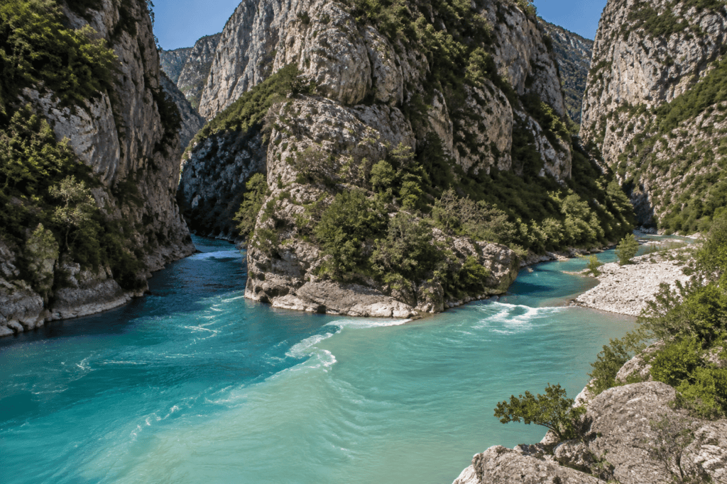 Deux cours d’eau aux teintes turquoise et vert pâle se rejoignent au pied de falaises calcaires.