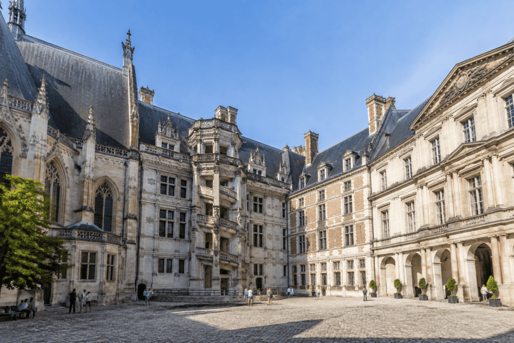 Dans la cour du château royal de Blois, des façades gothiques et Renaissance se font face, avec un escalier extérieur sculpté et une aile à arcades.
