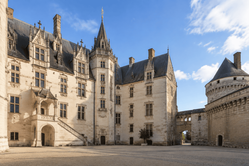 Cour pavée bordée de façades claires à fenêtres et détails sculptés, avec une tour ronde à droite.