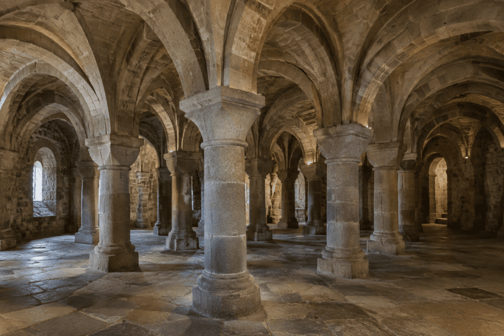 Une salle intérieure en pierre aux voûtes basses, soutenues par de nombreux piliers massifs.