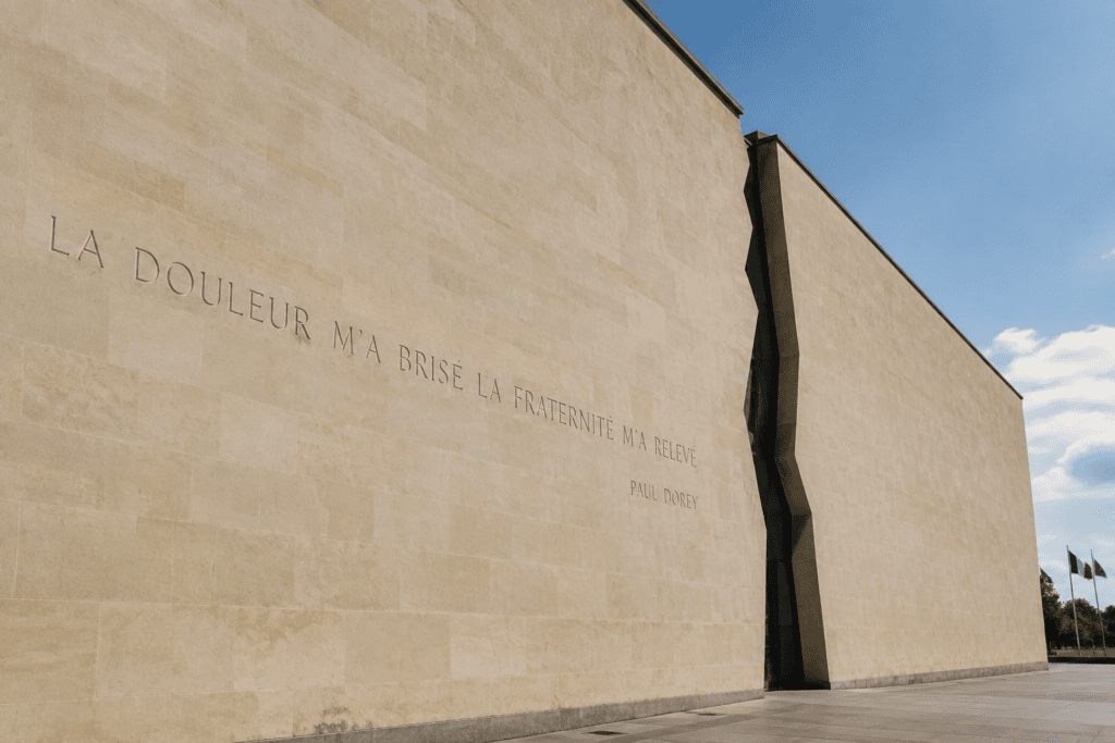 La façade en pierre claire du Mémorial de Caen, traversée par une profonde fracture verticale, porte l’inscription « La douleur m’a brisé, la fraterni