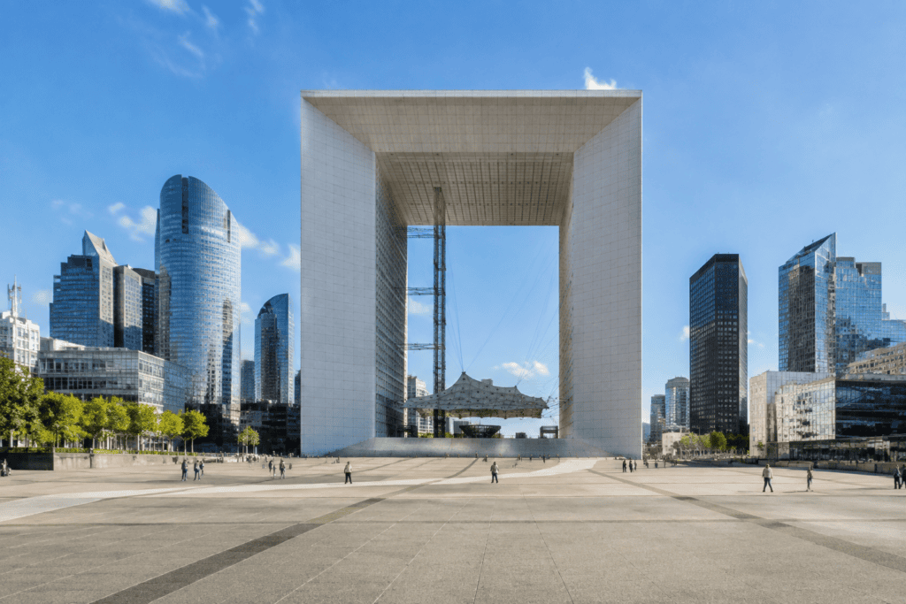 La Grande Arche encadrée par des tours, au fond d’un vaste parvis piéton sous un ciel dégagé.