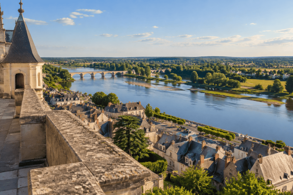Depuis une terrasse du château, la Loire et un pont à arches dominent les toits d’Amboise, avec une tour et un parapet de pierre au premier plan.