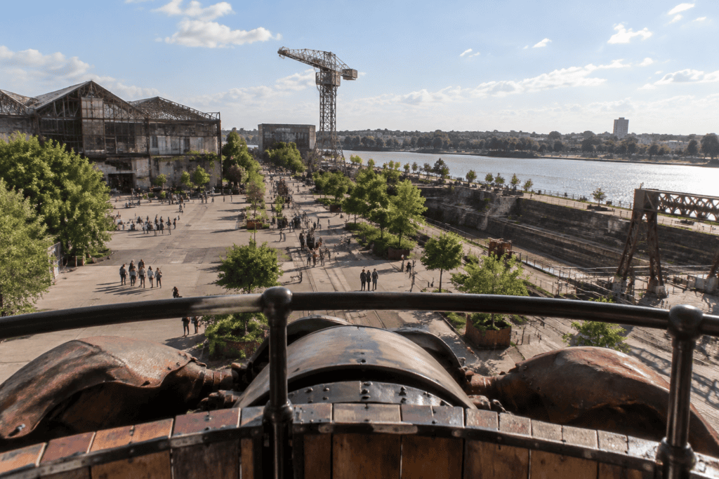 Vue depuis une structure mécanique sur une esplanade arborée, des bâtiments industriels et la Loire.