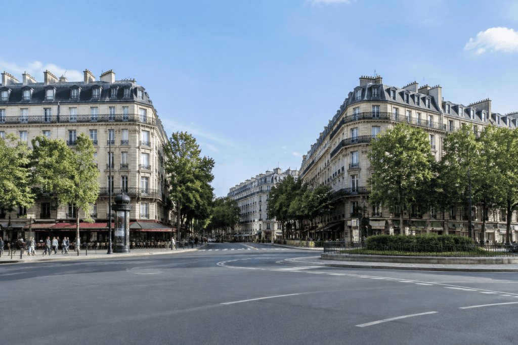 Vue d’un large carrefour parisien, bordé d’immeubles haussmanniens et d’arbres.