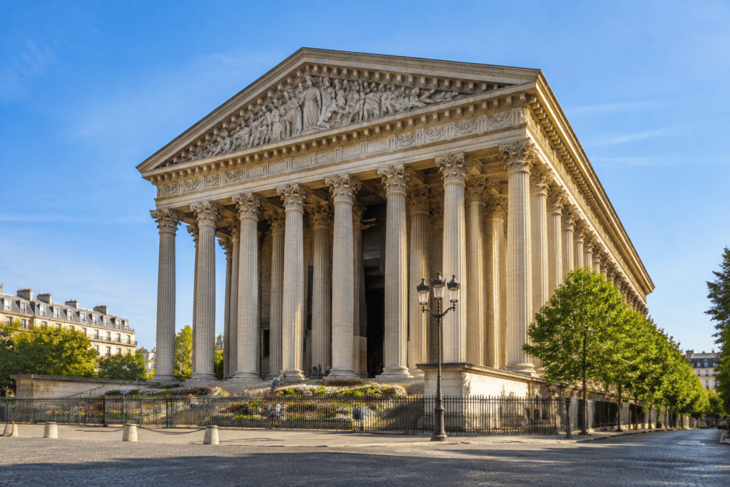 Église à façade ornée et colonnes, vue depuis une place pavée sous un ciel dégagé.