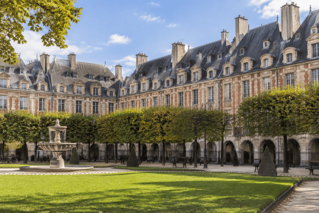 Jardin bordé de pelouses et d’arbres devant les arcades et les façades à toits d’ardoise de la place des Vosges.