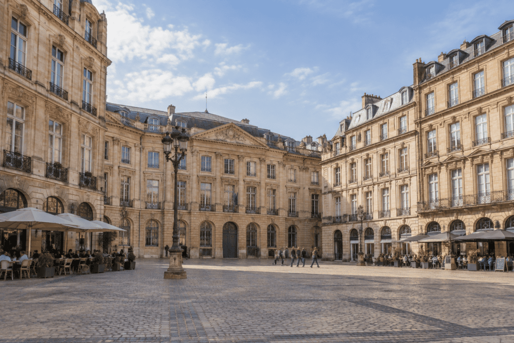 Place pavée bordée de façades classiques et de terrasses de café.