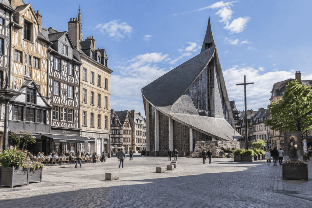 L’église Sainte-Jeanne-d’Arc, aux toits courbes et à la grande croix, se dresse sur la place pavée du Vieux-Marché, bordée de maisons anciennes.