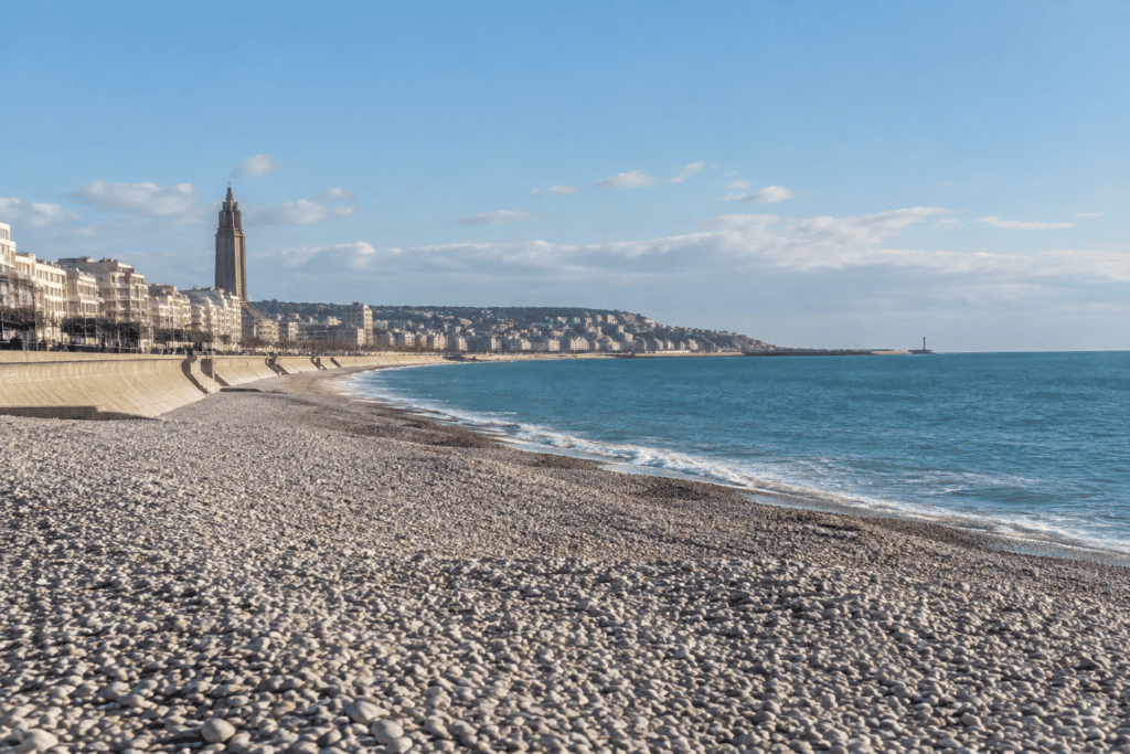 Plage de galets au Havre, avec la digue, des bâtiments du front de mer et la mer.