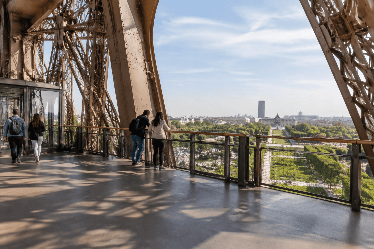 Des visiteurs se tiennent près de la rambarde d’une plateforme de la Tour Eiffel, face au Champ-de-Mars.