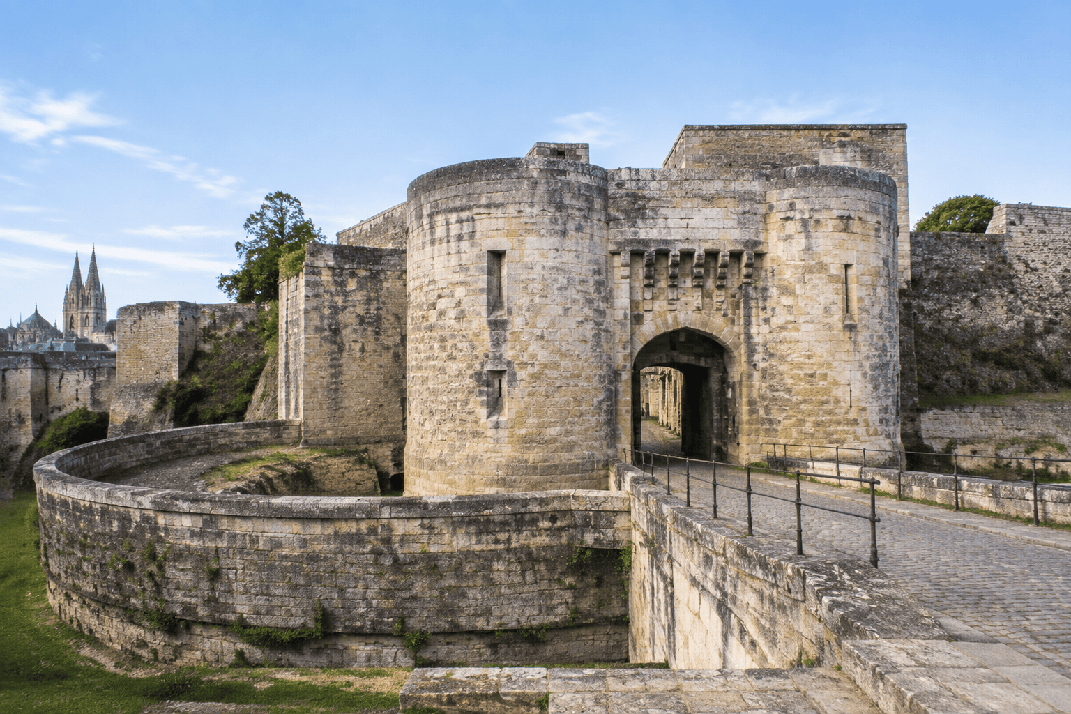 Passage voûté encadré de tours de pierre, relié à une chaussée pavée et entouré d’une enceinte fortifiée.