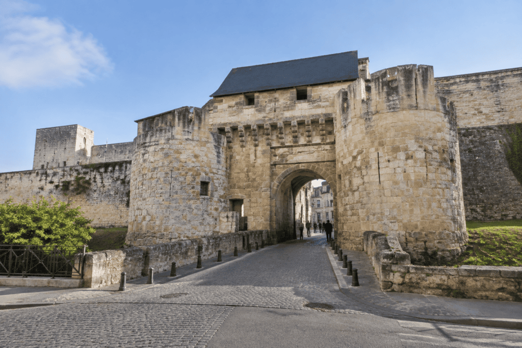 Arche d’une entrée fortifiée encadrée de tours rondes et de courtines en pierre, avec une voie pavée au premier plan.