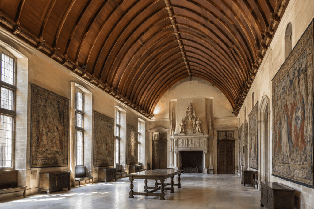 Salle historique aux murs ornés de tapisseries, avec une haute voûte en bois, une table centrale et une cheminée au fond.