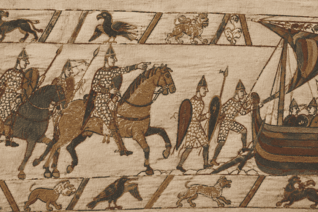 Détail de la Tapisserie de Bayeux montrant des personnages en armure, des chevaux et un navire.