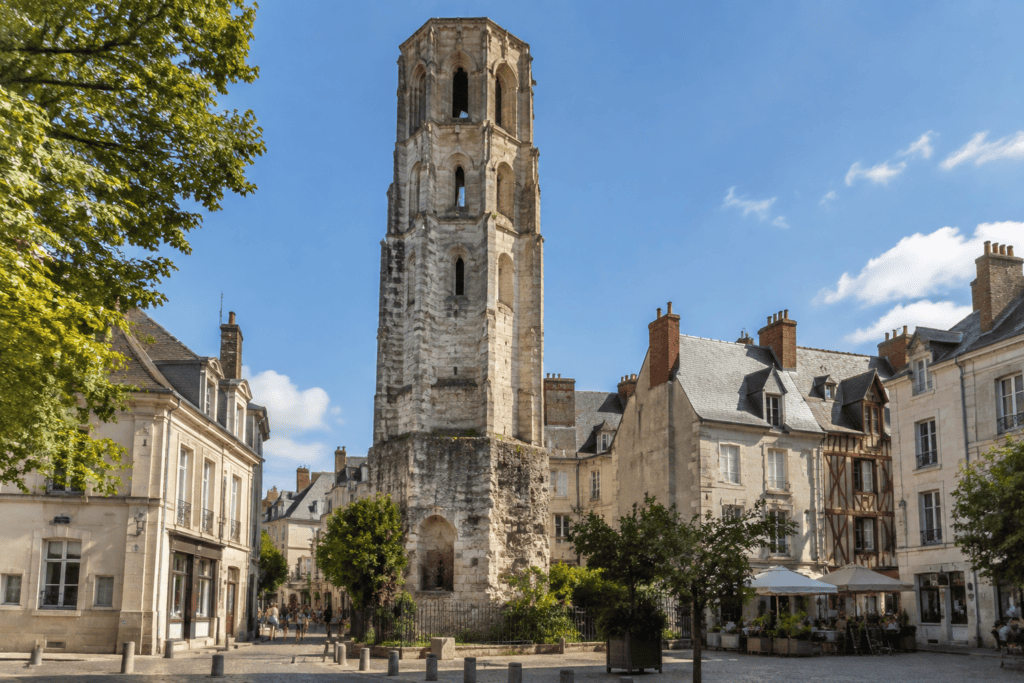 Une haute tour de pierre se dresse parmi les bâtiments et les arbres du centre ancien de Tours.