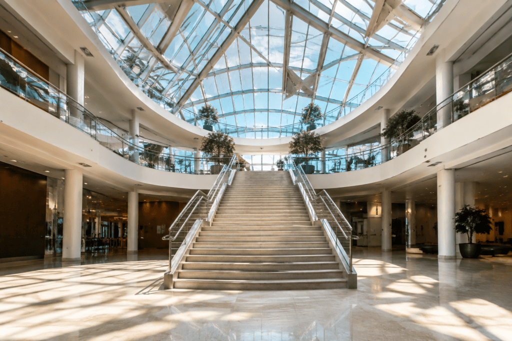 Atrium lumineux sous une verrière, avec un large escalier central et des galeries à l’étage.