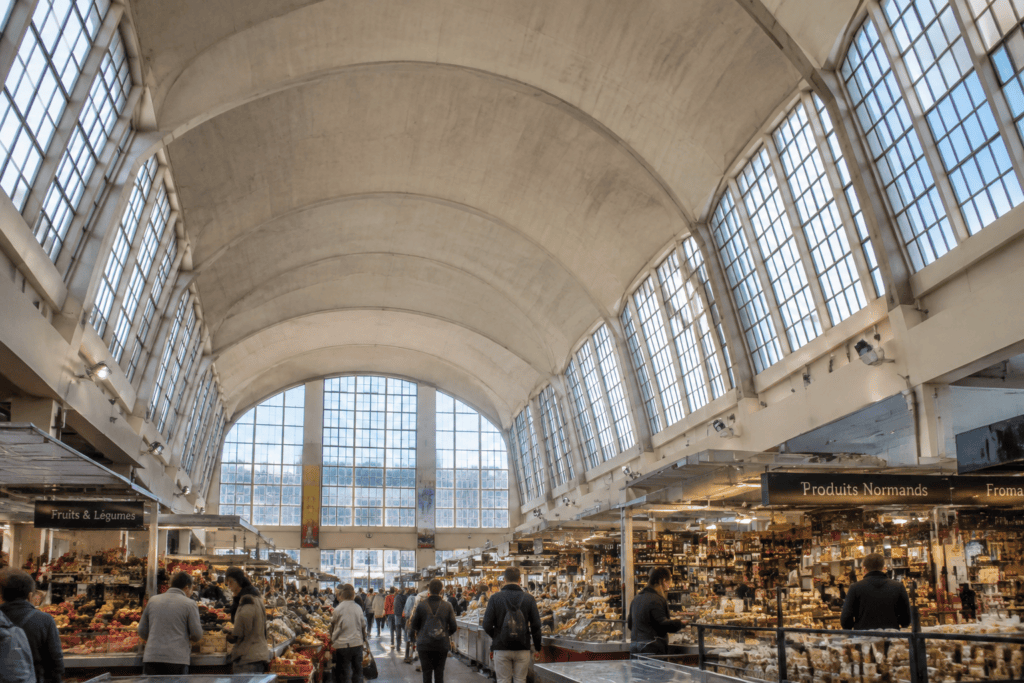 Vue intérieure d’une halle de marché à couverture voûtée, avec de hautes fenêtres, des étals et des visiteurs.