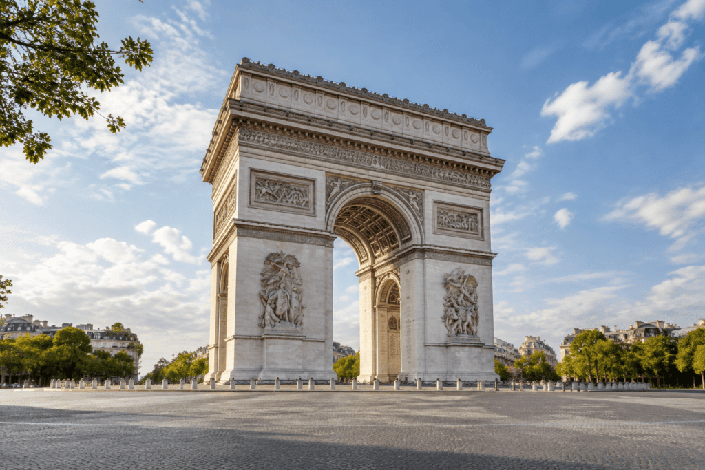 L’Arc de Triomphe vu de face, avec ses sculptures, les arbres alentour et une avenue au premier plan.