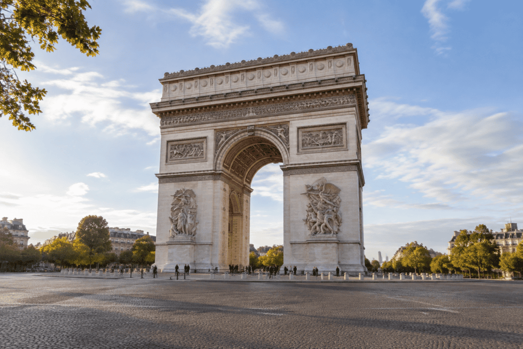 L’Arc de Triomphe se dresse au centre d’une vaste place pavée, avec des arbres et des avenues en arrière-plan.