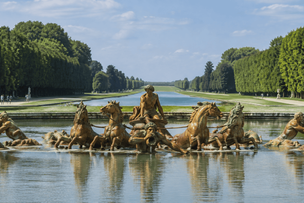 Le groupe sculpté d’Apollon et des chevaux s’élève au-dessus du bassin, avec un long canal et des rangées d’arbres en arrière-plan.