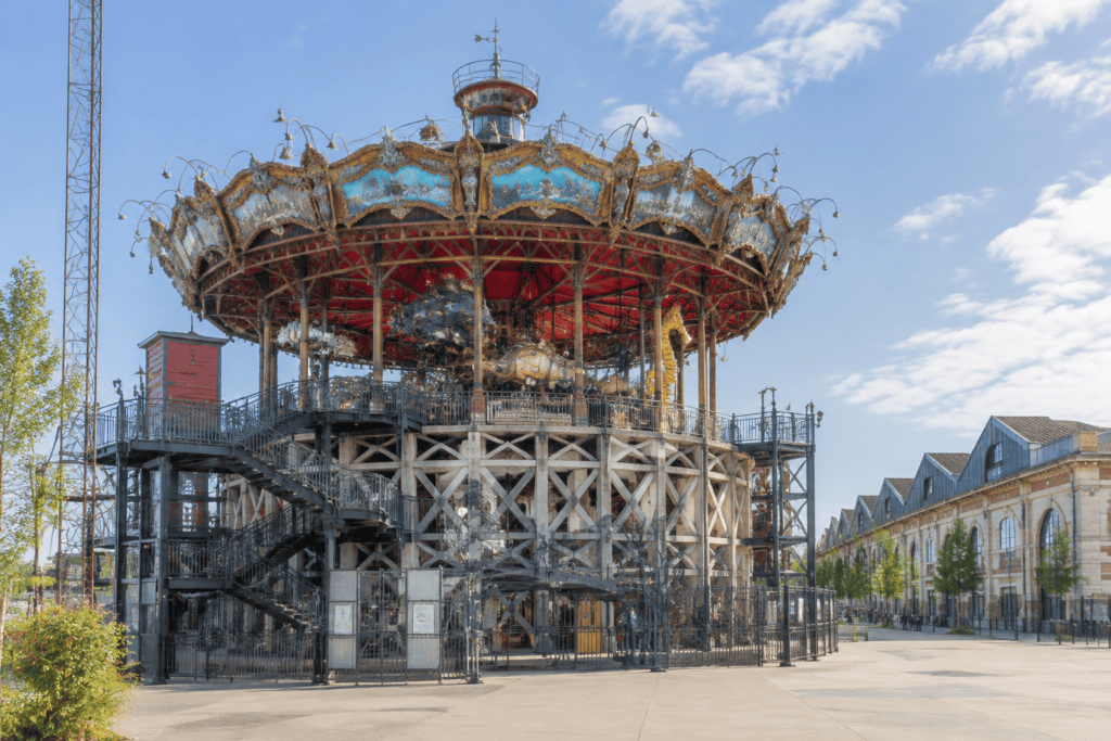 La structure circulaire surélevée du Carrousel des Mondes Marins, avec ses escaliers et ses ornements, se dresse devant un bâtiment industriel.