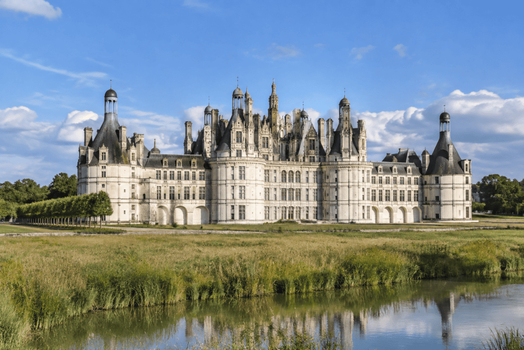 Façade du château de Chambord derrière un plan d’eau bordé de végétation.
