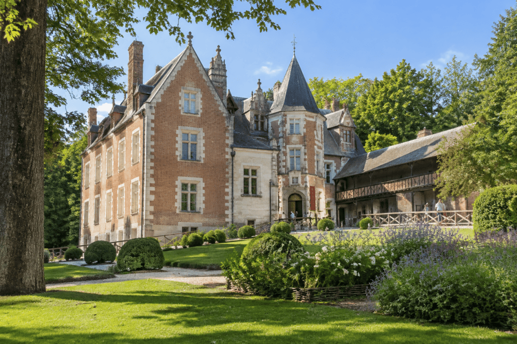 Façade du Clos Lucé, avec sa tour à toit d’ardoise, son bâtiment à colombages et son jardin fleuri.