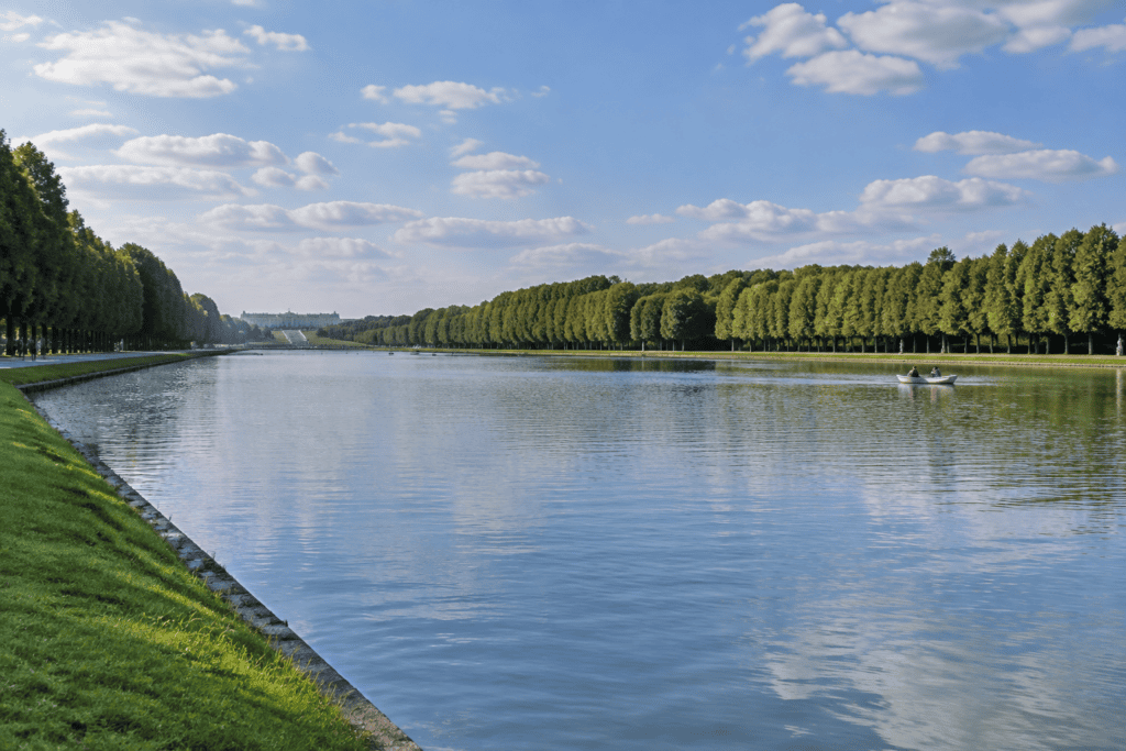 Large canal bordé de pelouses et de longues rangées d’arbres, avec une petite embarcation sur l’eau.