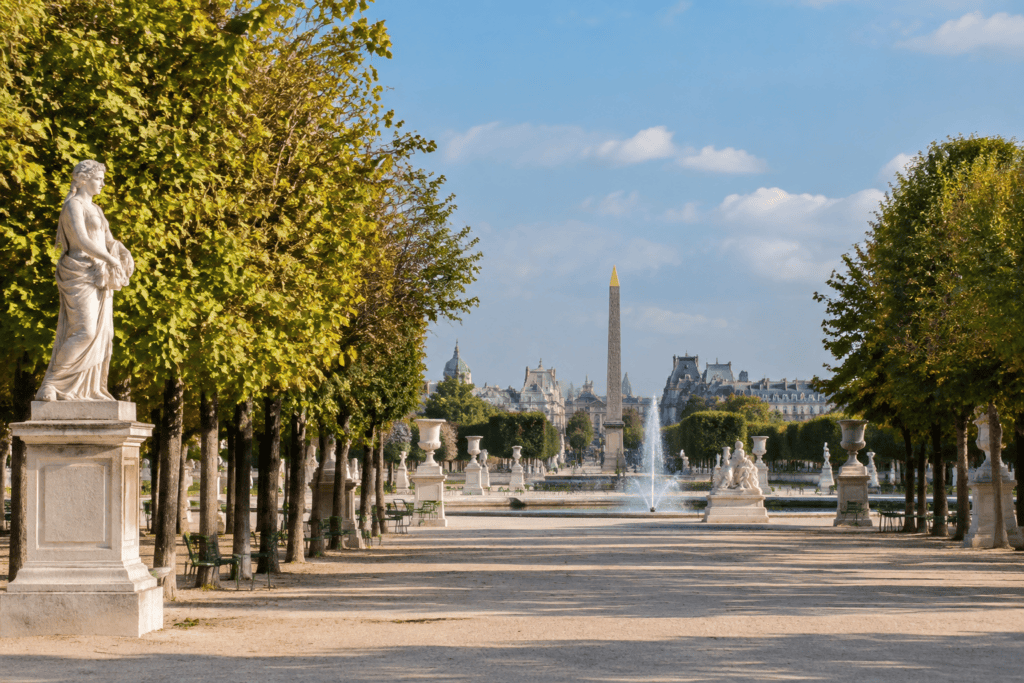 Allée bordée d’arbres et de statues, avec des bassins et un obélisque visible au loin.