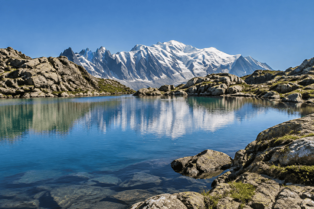 Un lac de montagne reflète des sommets enneigés, entouré de rives rocheuses.