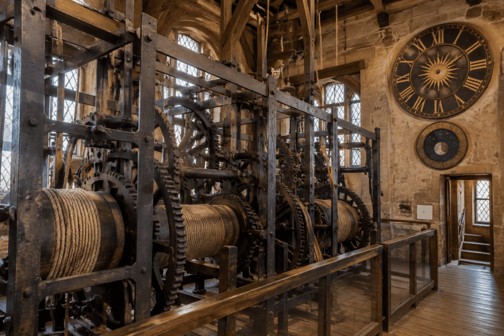Grand mécanisme à engrenages et cordages dans une salle en pierre, avec deux cadrans fixés au mur.