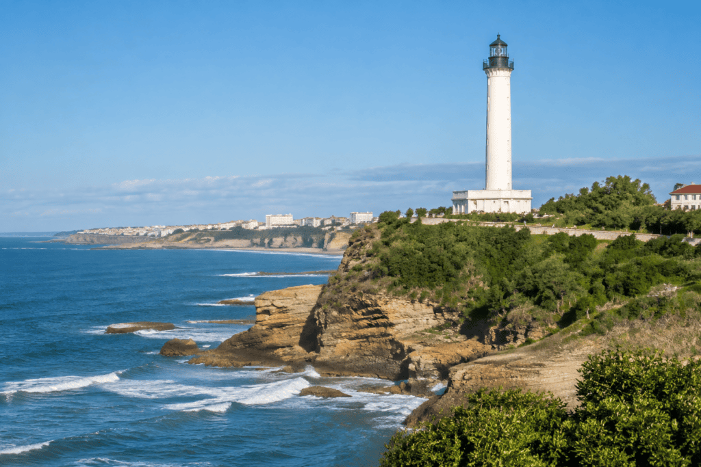 Un phare blanc se dresse sur un promontoire verdoyant au-dessus de l’océan et des falaises.
