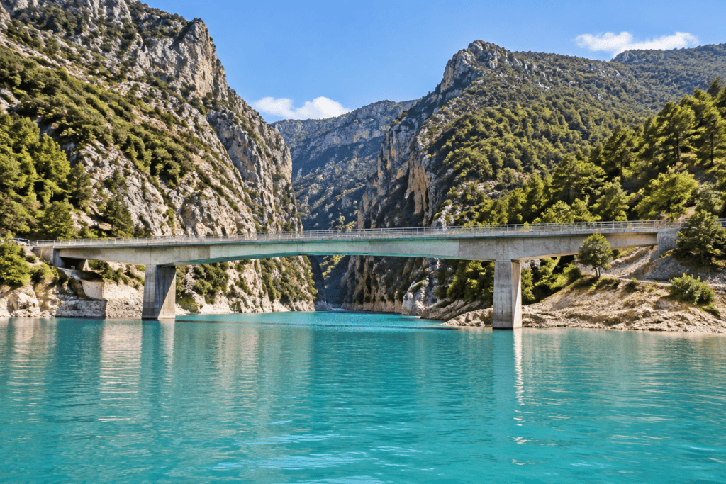 Un pont en béton traverse l’eau turquoise entre les falaises boisées des gorges.