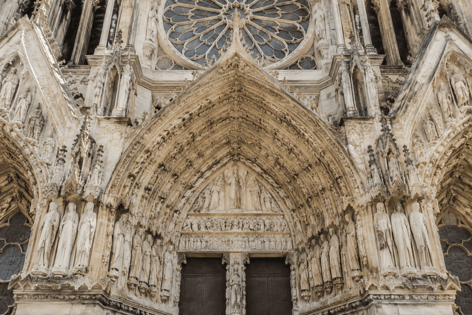 Le portail central gothique, ses statues et ses reliefs sous la grande rose de la cathédrale de Reims.