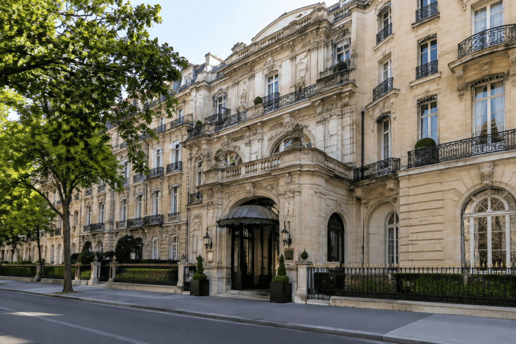 Façade en pierre ornée, avec un grand portail couvert et des balcons en fer forgé, le long d’une rue parisienne.