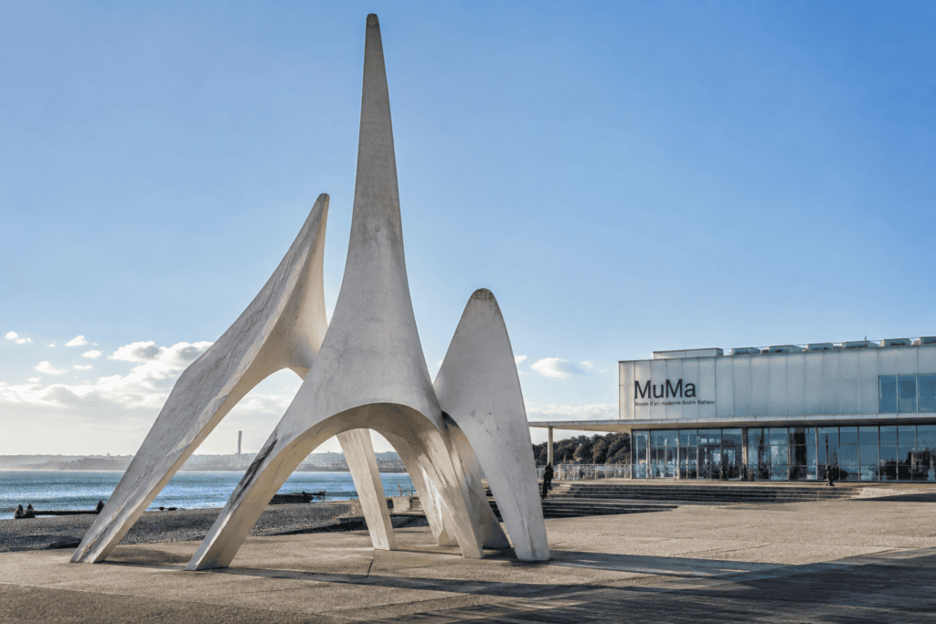 La sculpture aux hautes formes courbes de Le Signal se dresse devant le MuMa, avec le front de mer visible à gauche.