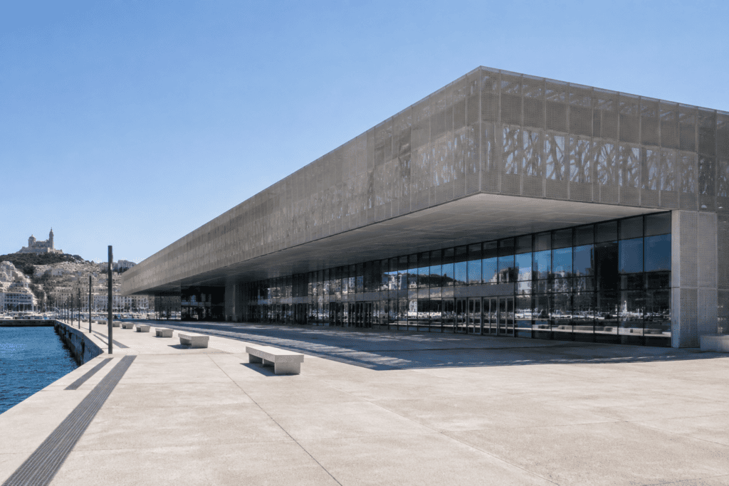 Long bâtiment contemporain du MuCEM, avec une façade en béton ajouré et des baies vitrées donnant sur une esplanade au bord de l’eau.