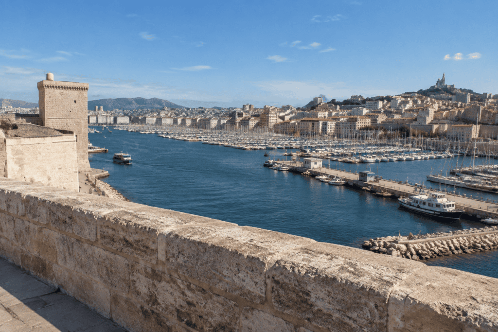 Un parapet de pierre et une tour du fort Saint-Jean dominent les bassins du Vieux-Port, les quais et les immeubles de Marseille.