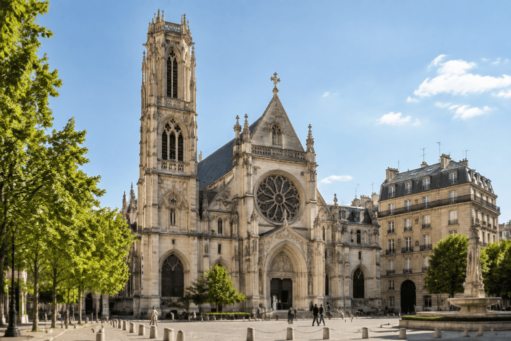 Façade gothique de l’église Saint-Germain-l’Auxerrois, avec sa tour et sa rosace, sur une place arborée.