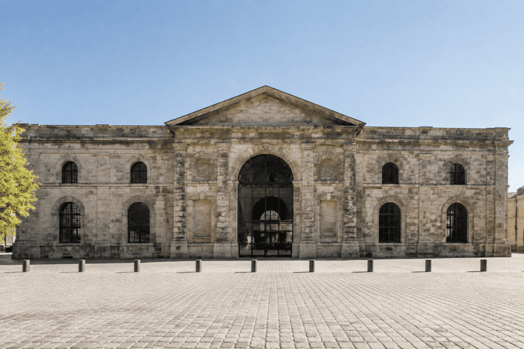 Façade symétrique en pierre avec une large entrée voûtée et une place pavée au premier plan.