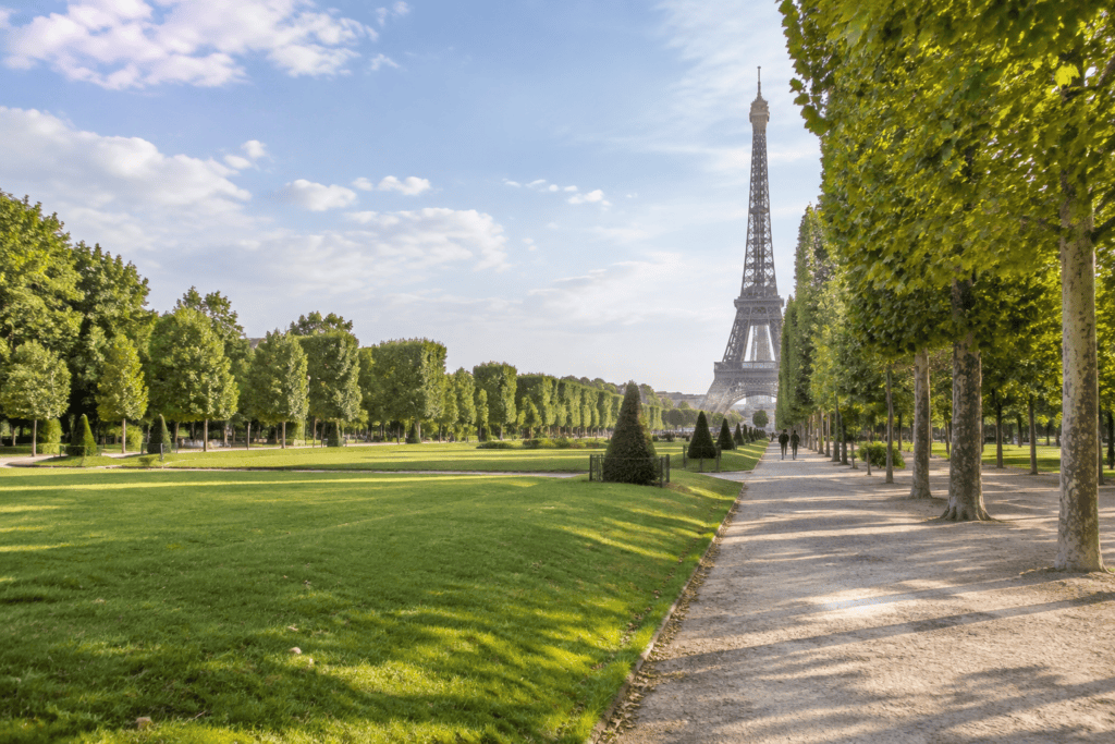 Une large pelouse et une allée bordée d’arbres s’étendent vers la Tour Eiffel, visible au loin.